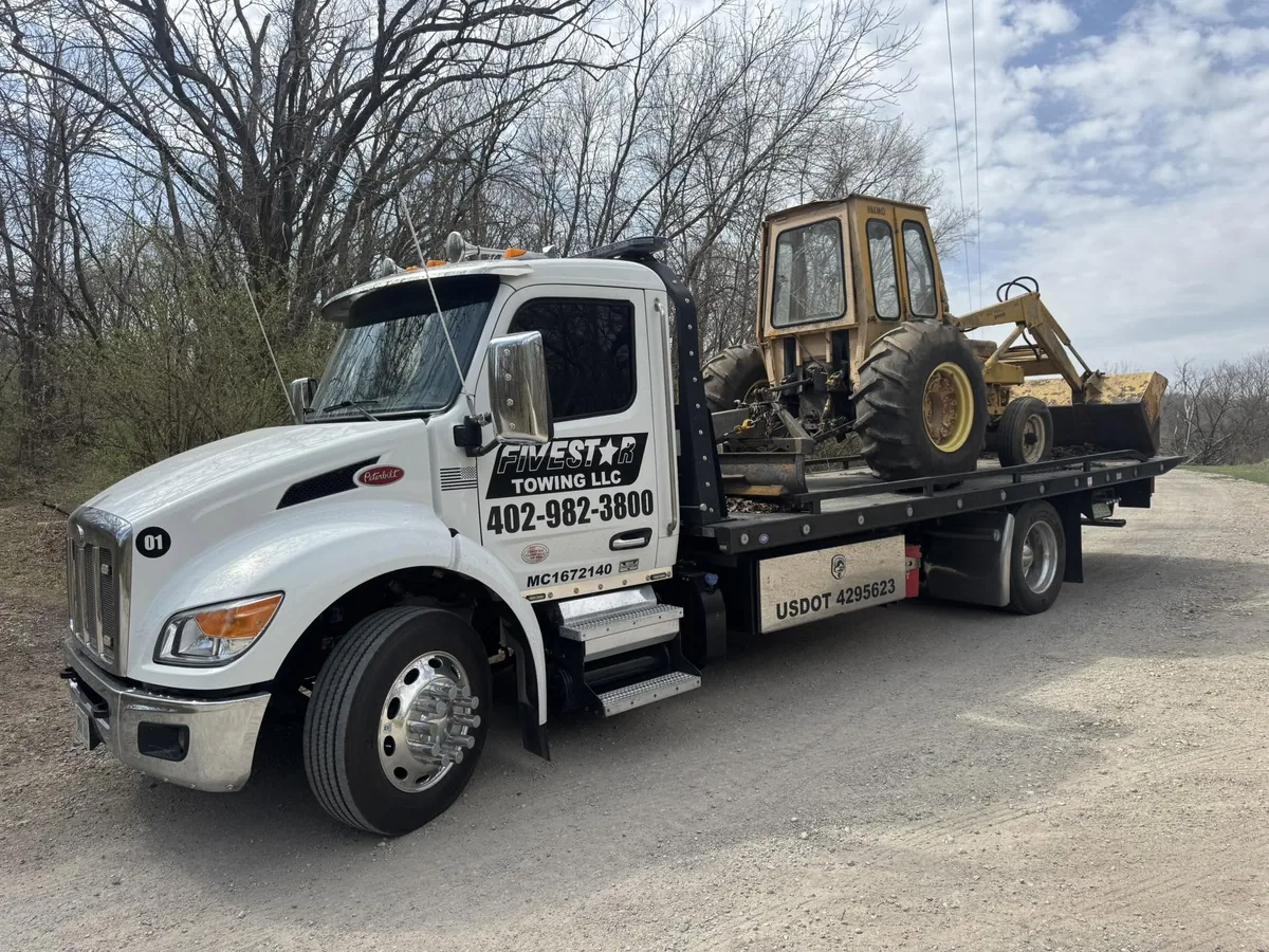 Tow truck hauling a yellow backhoe loader
