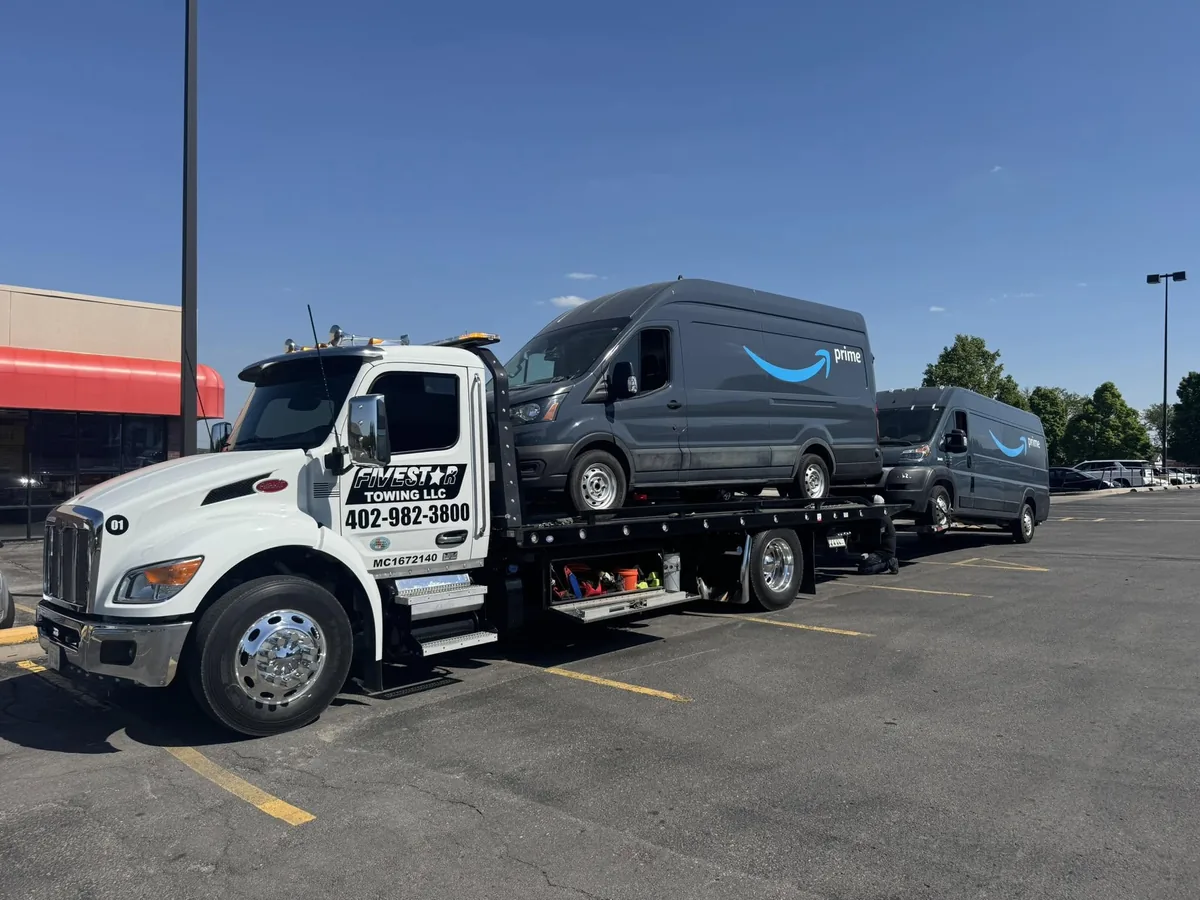 Flatbed tow truck hauling a blue Amazon delivery van strapped to the deck