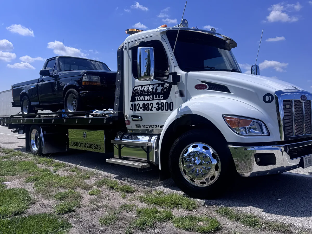 Flatbed tow truck loaded with a dark pickup truck