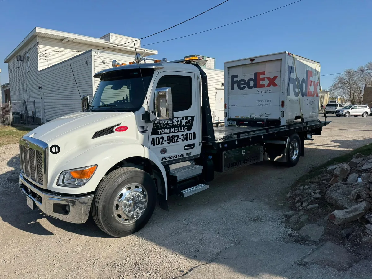 Flatbed tow truck loaded with a FedEx box truck secured to the deck