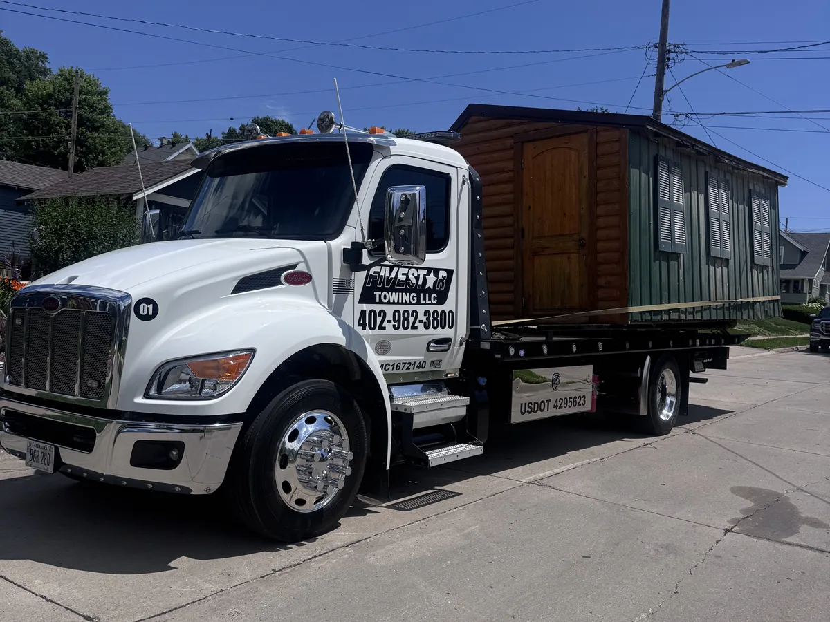 Flatbed tow truck hauling a wooden storage shed