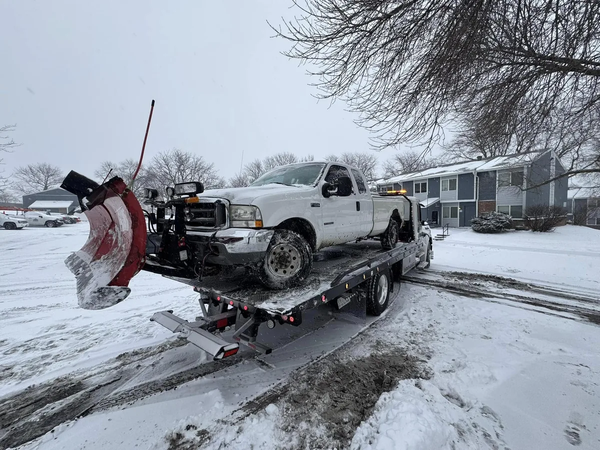 Tow truck fitted with a front snow plow blade clearing a snow covered street