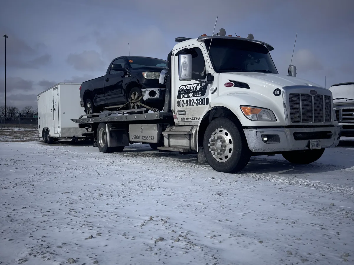 Flatbed tow truck loading a car on a snow covered lot