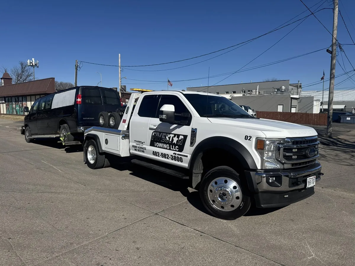 Integrated wrecker towing a black cargo van from a city street