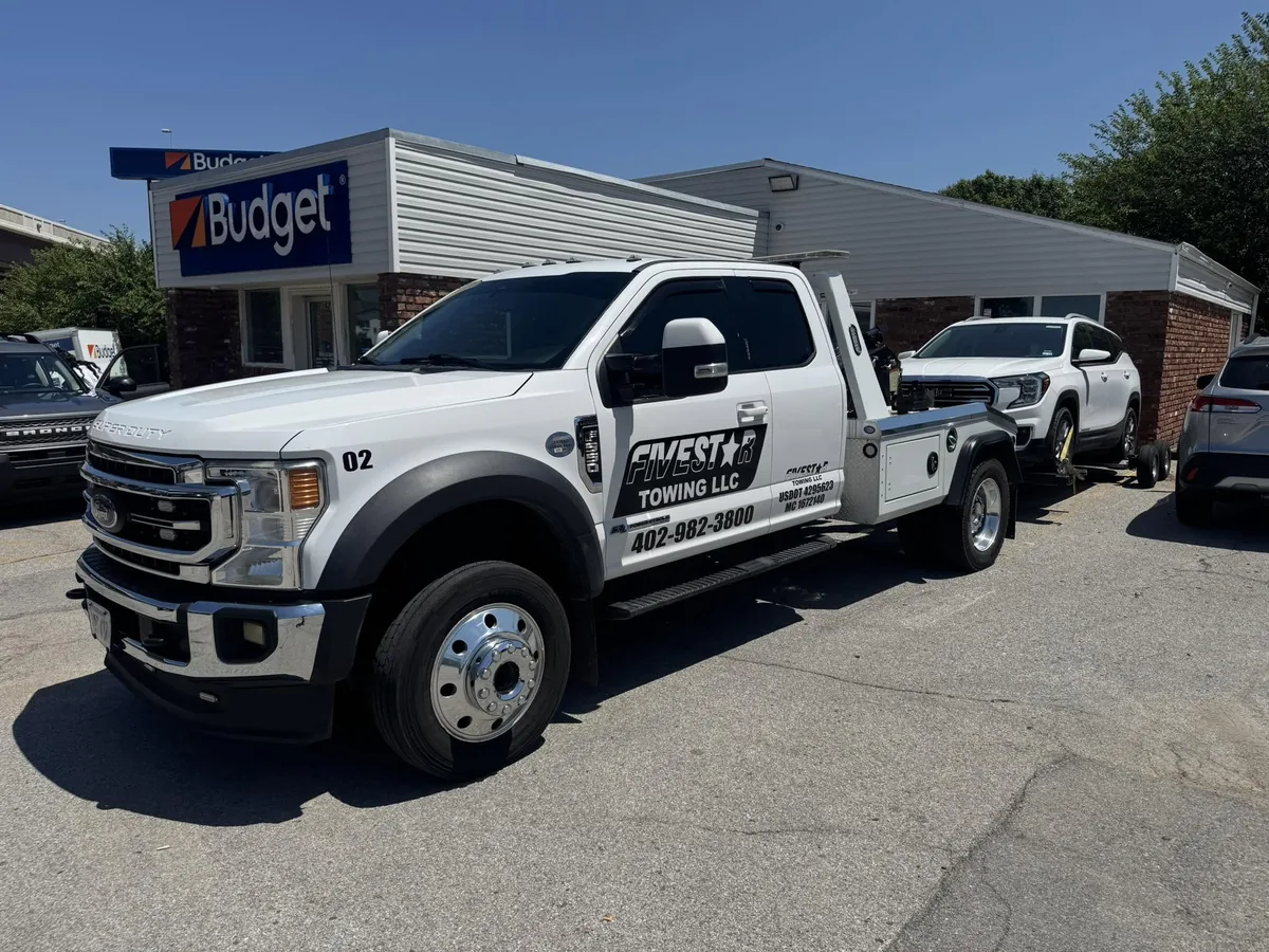 Integrated wrecker towing a white pickup truck out of a lot